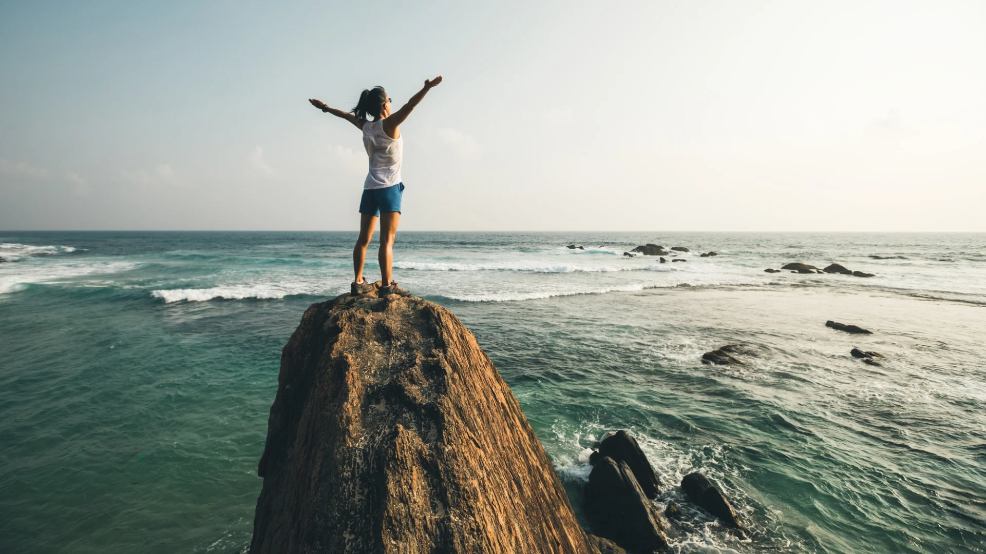 An athlete stands on top of a seaside cliff she has just climbed