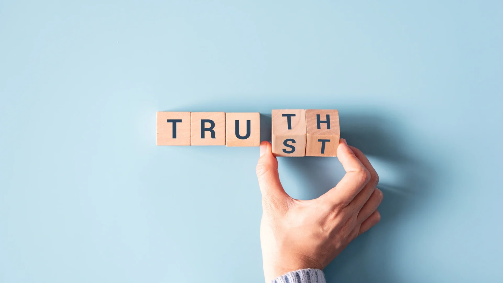 Blocks lined out that spell TRUTH with a hand turning the last two letters to spell TRUST