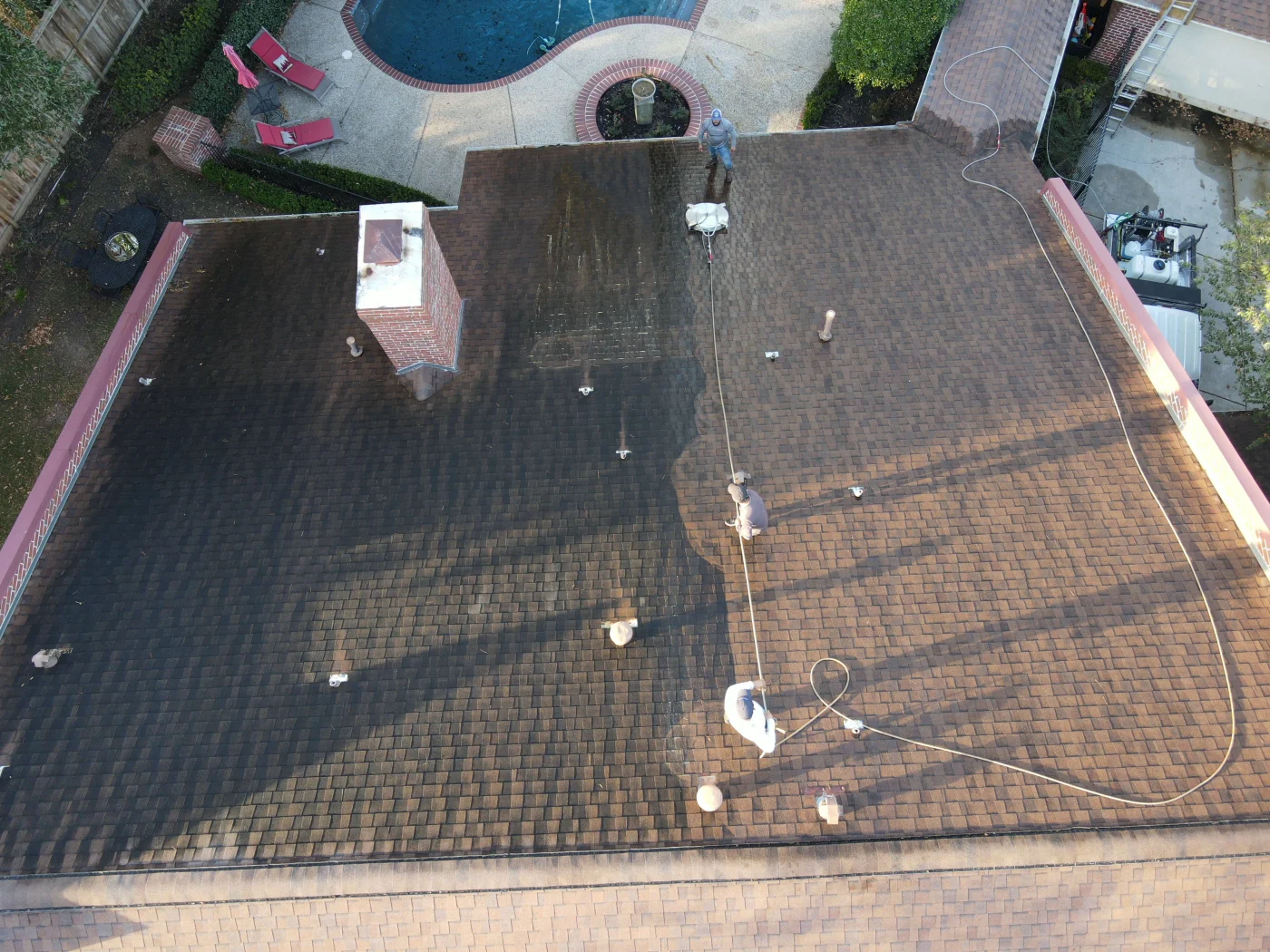 Professional Roof Cleaning | Conroe, TX | Brinkmann Quality Roofing Professional roof cleaning in Conroe, TX, with workers pressure washing darkened shingles to restore appearance near a backyard pool.