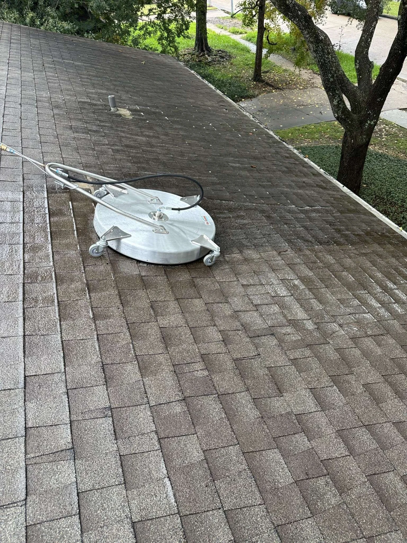 Thorough Roof Cleaning | Conroe, TX | Brinkmann Quality Roofing Close-up of roof cleaning in Conroe, TX, with a professional surface cleaner restoring asphalt shingles, performed by Brinkmann Quality Roofing.