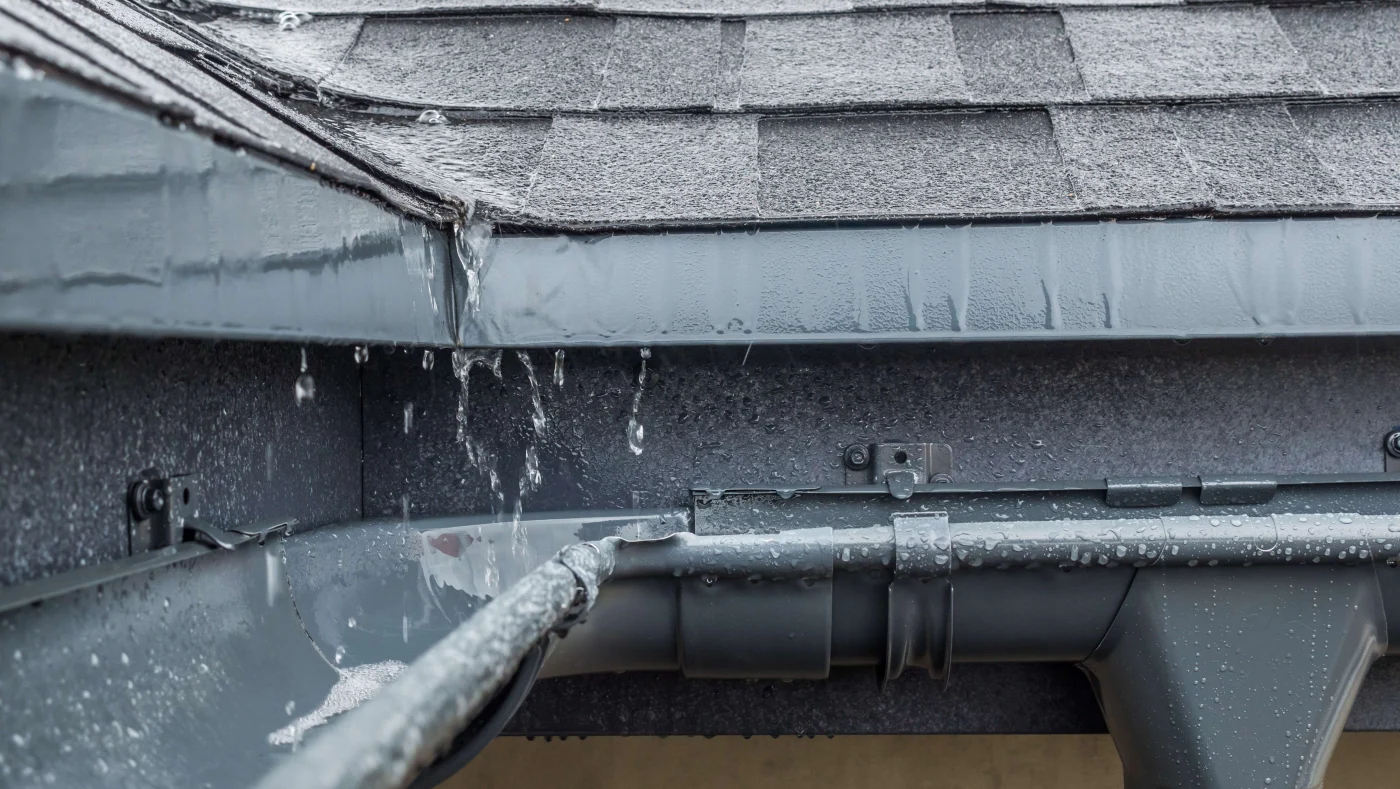 Trusted Roof Repairs in League City, TX | Brinkmann Quality Roofing A close-up on rain gutters beside a shingle roof during a rain storm.