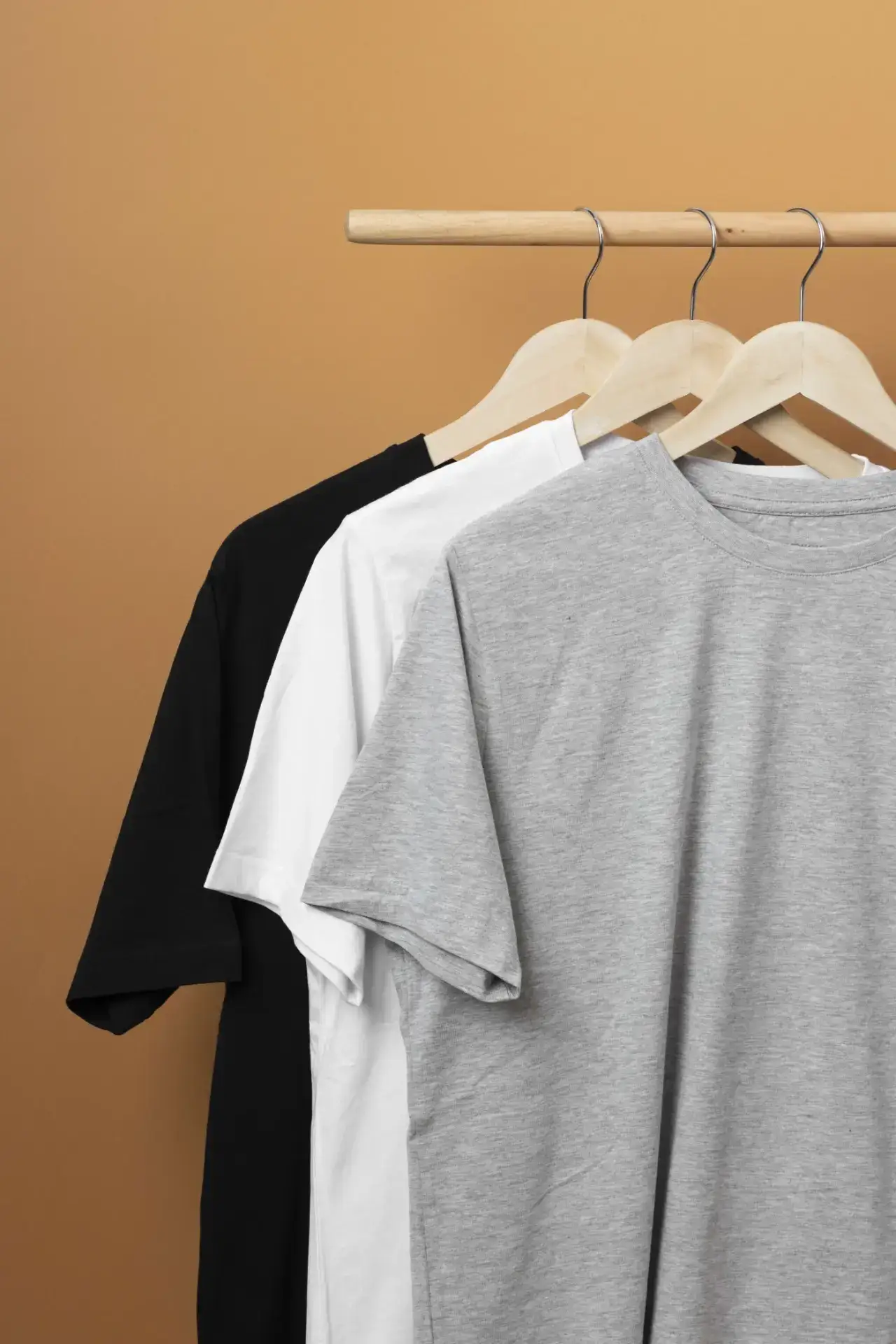 Plain white, black, and gray shirts on hangers on a rack against a plain orange-yellow background
