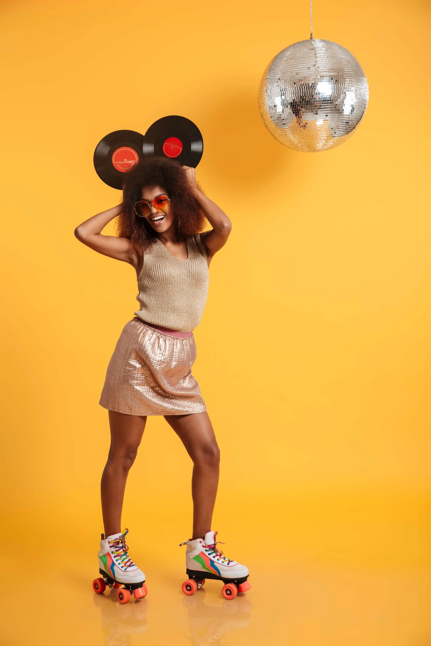 Full Length Portrait Of A Happy Laughing Afro American Woman A young woman wearing rollerskates and holding vinyl records against a yellow background with a disco ball