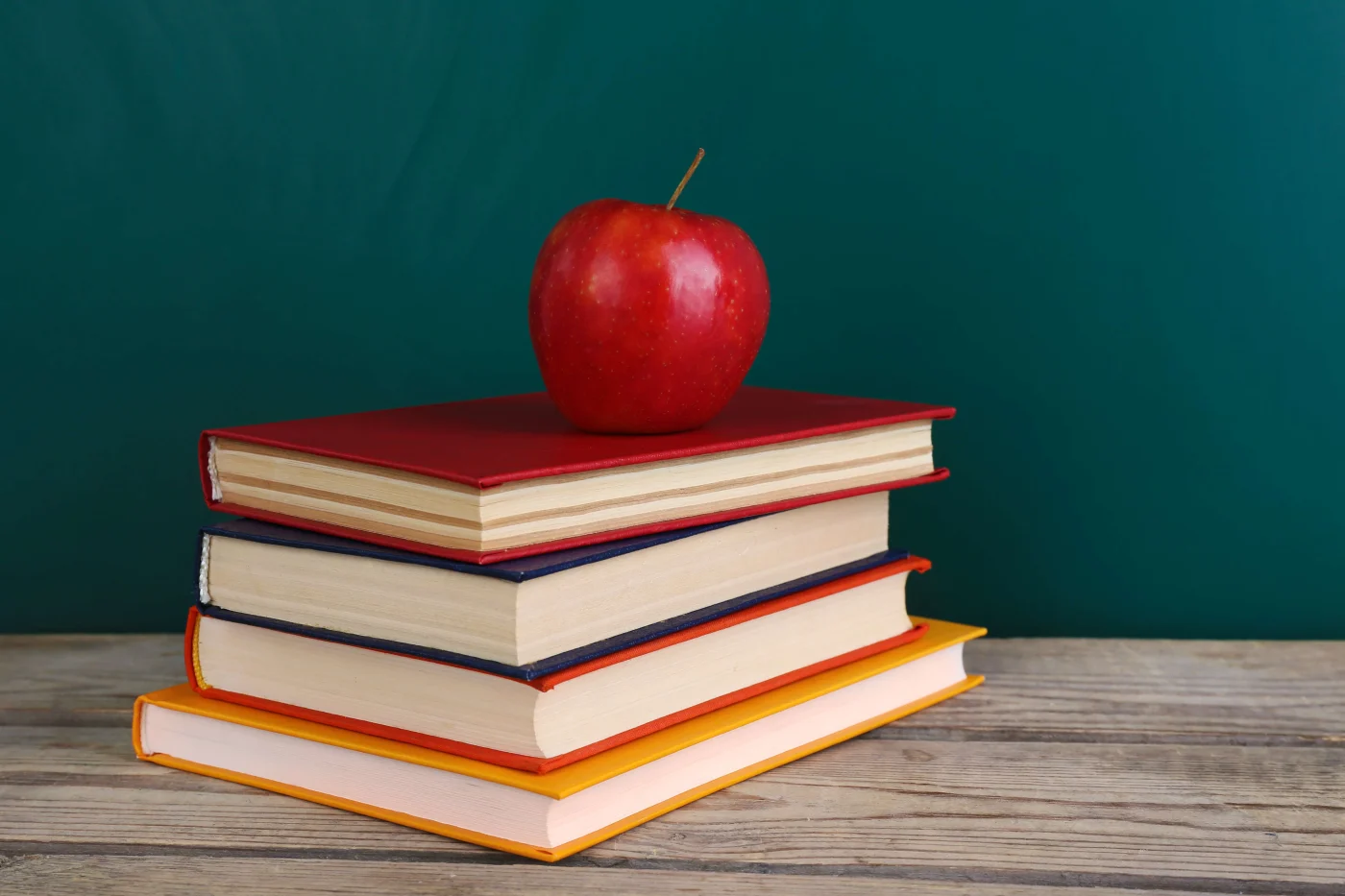 Informative Residential Roofing in the Houston Area | Brinkmann Quality Roofing Services A stack of books topped with a red apple against a blackboard.