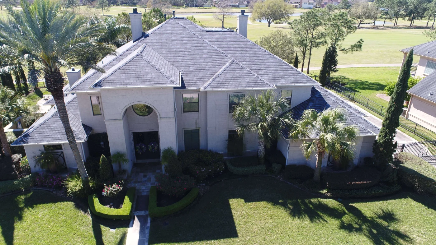 Dcim100mediadji 0013.jpg An aerial view of a large Friendswood, TX home with a gray shingle roof, multiple gables, chimneys, palm trees, and manicured landscaping.