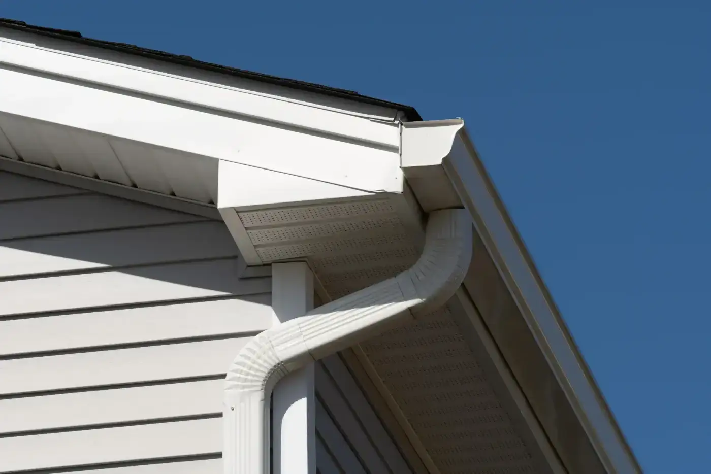 Dependable Gutters & Downspouts | Katy, TX | Brinkmann Quality Roofing Services Clean white vinyl siding and soffits frame an expertly installed drainage system built by professional gutter and downspout services.