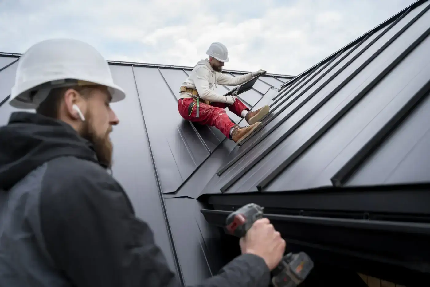 Excellent Gutters & Downspouts | Baytown, TX | Brinkmann Quality Roofing Services Two roofing technicians collaborate on a standing seam metal roof to deliver professional gutter and downspout services.