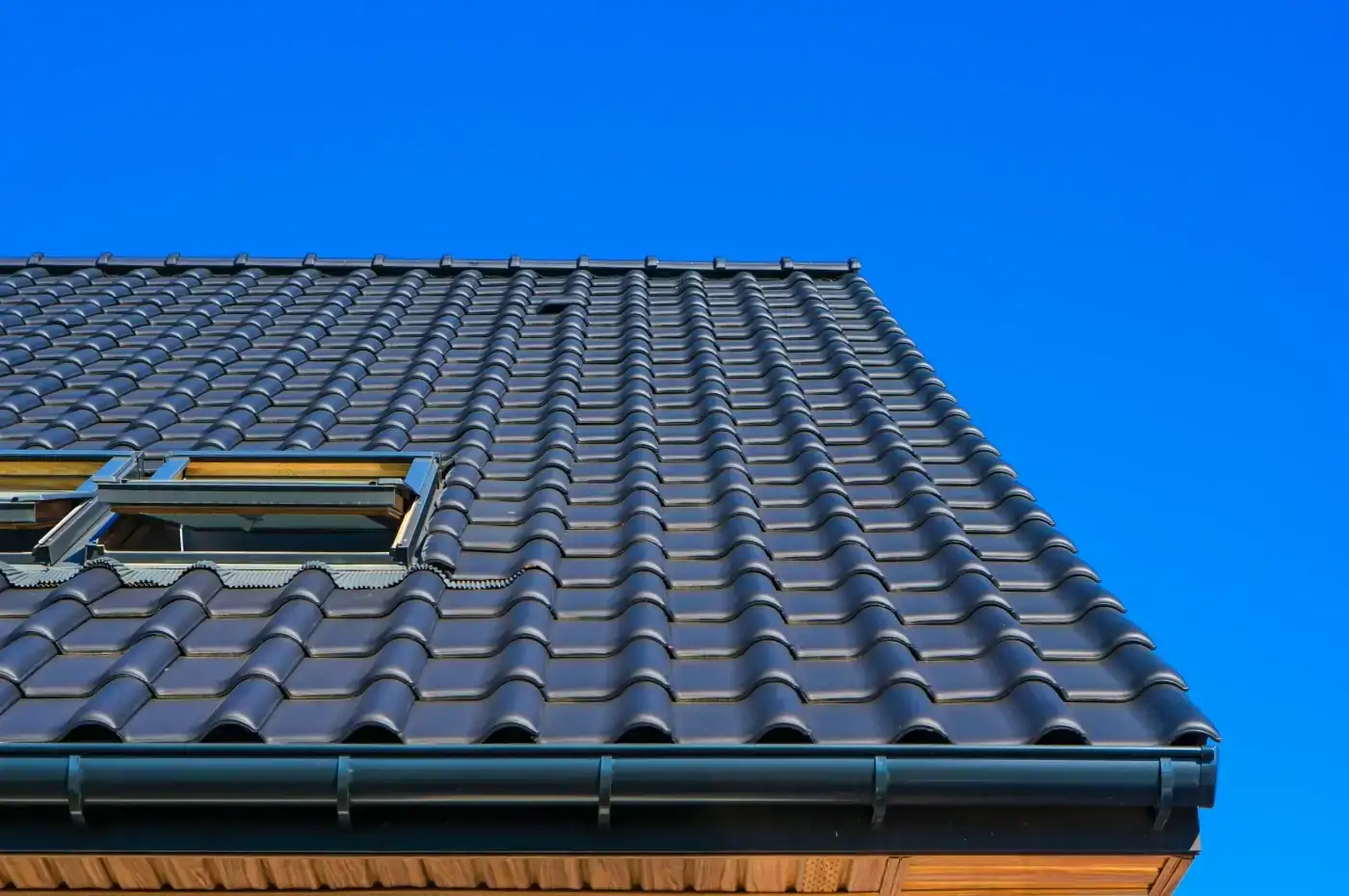 Fantastic Gutters & Downspouts | Baytown, TX | Brinkmann Quality Roofing Services Dark tile roofing with skylights features a newly installed drainage channel completed by professional gutter and downspout services.