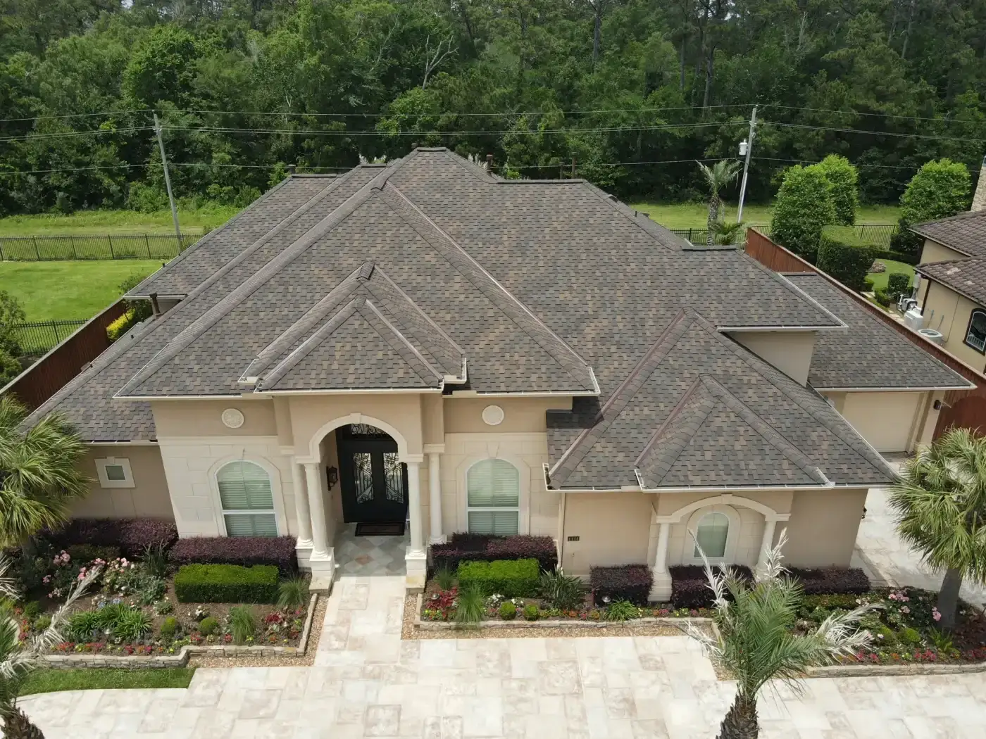 Premier Roof Replacement | West University, TX | Brinkmann Quality Roofing Services An aerial view displays a multi-gabled suburban estate boasting fresh architectural shingles installed as part of a total roof replacement.