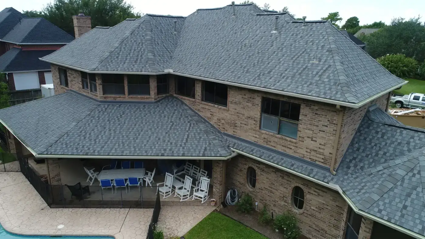 Superior Roof Replacement | West University, TX | Brinkmann Quality Roofing Services An elevated perspective captures a multi-level brick home featuring a complete shingle roof replacement over the patio and main structure.