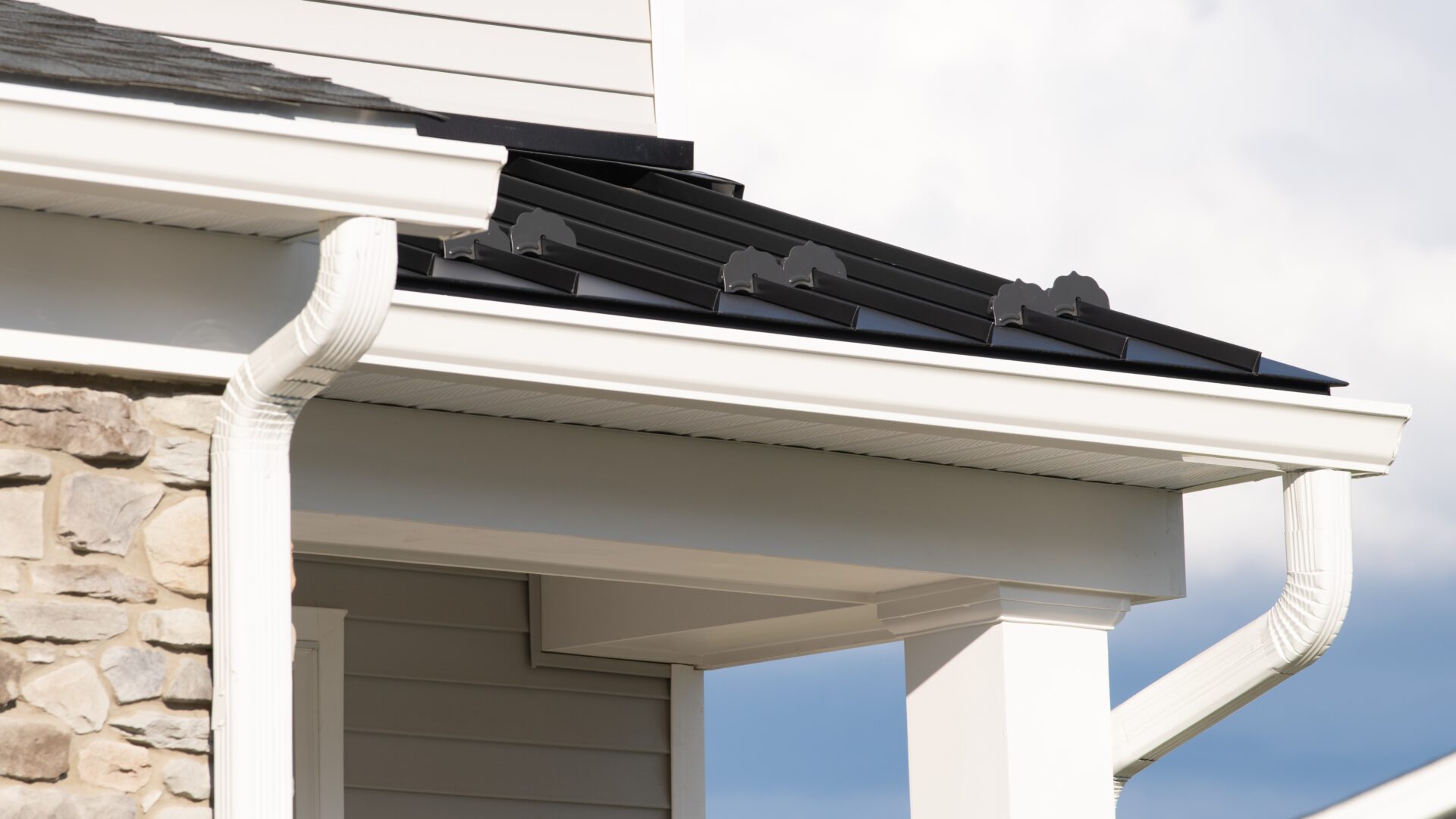 Closeup of a gutter downspout on a home with stone siding and a black metal roof