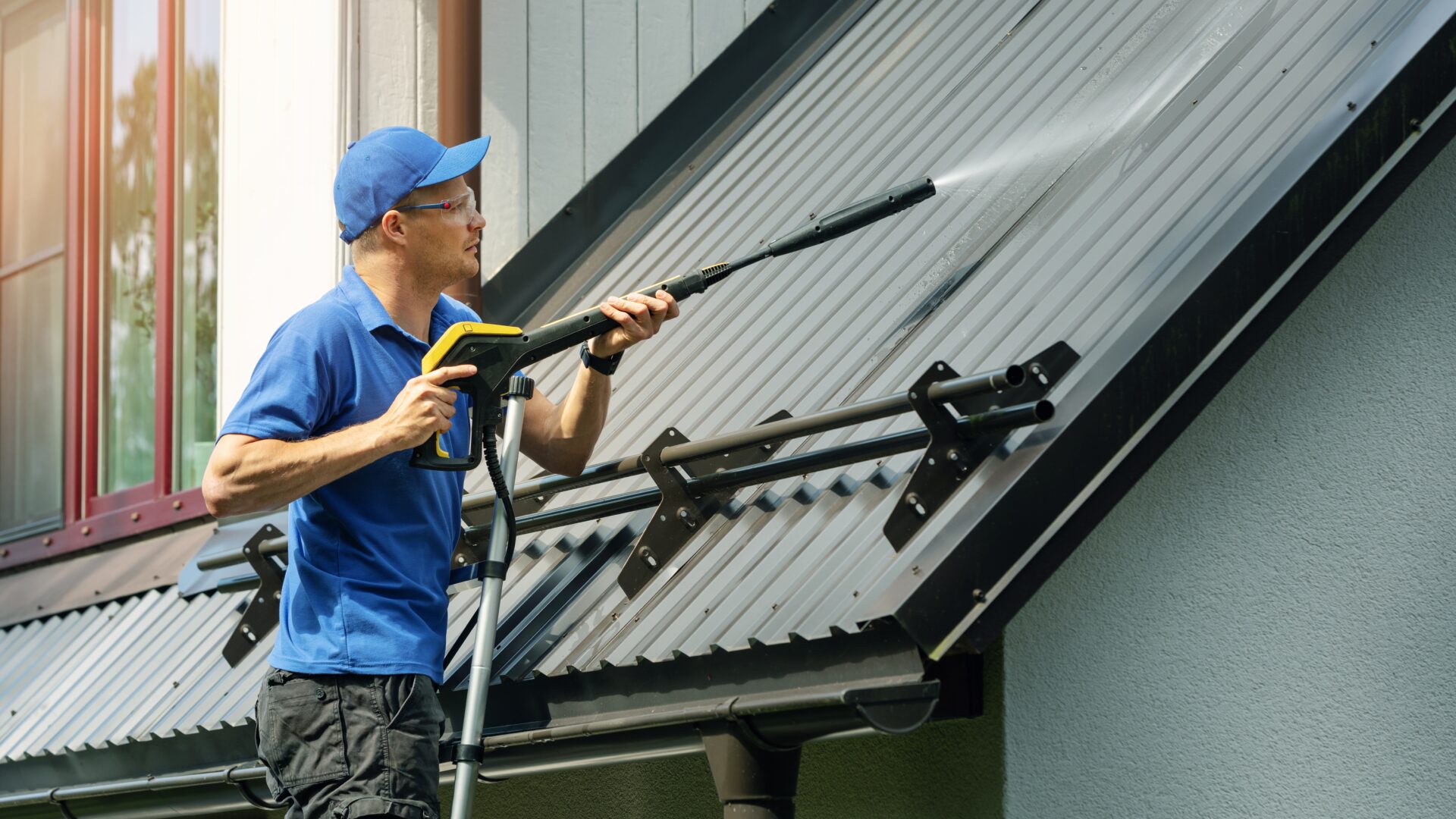 A roofer cleans a metal roof with a high-pressure hose