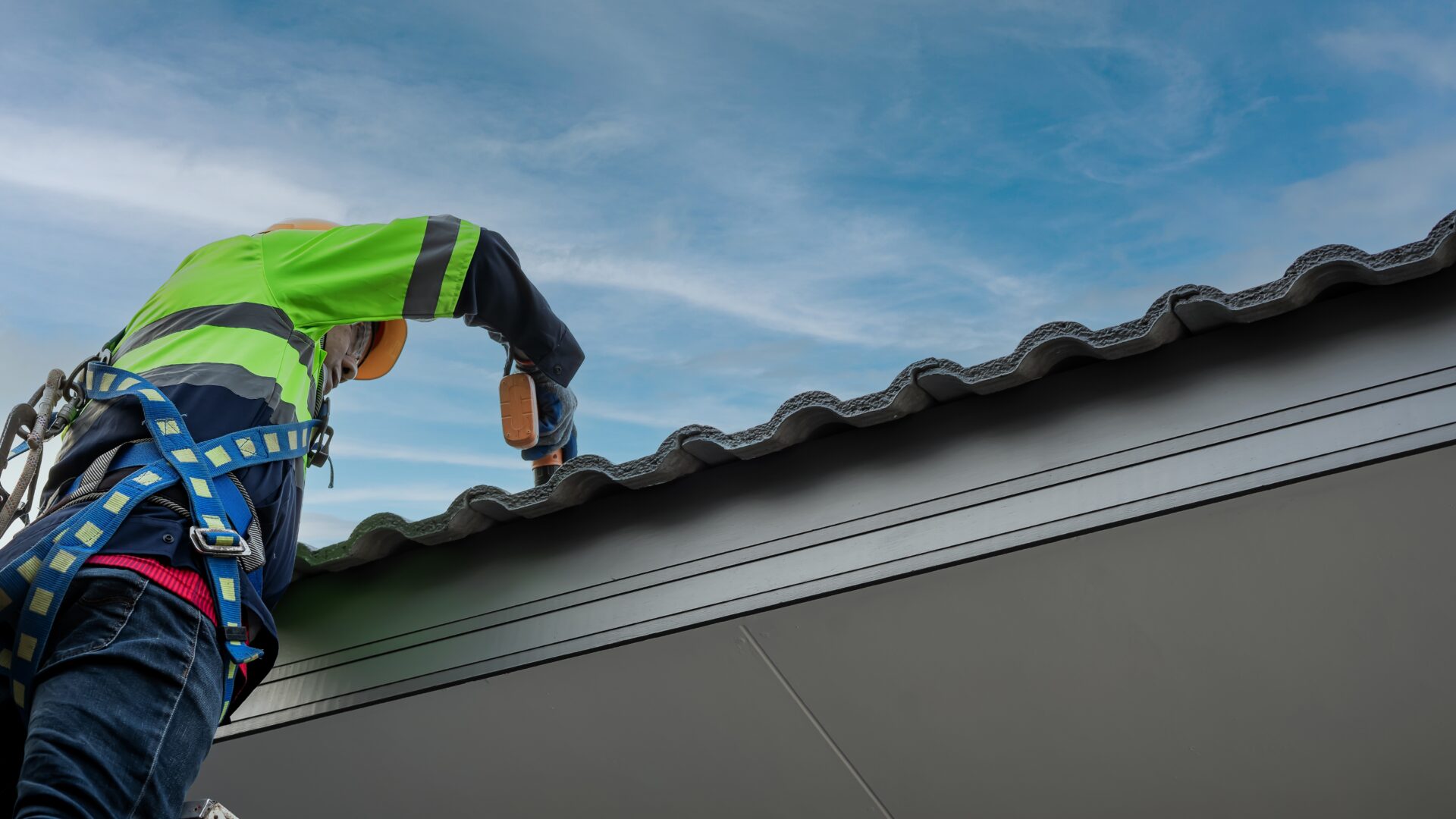 A roofer on a ladder makes repairs to a tile roof