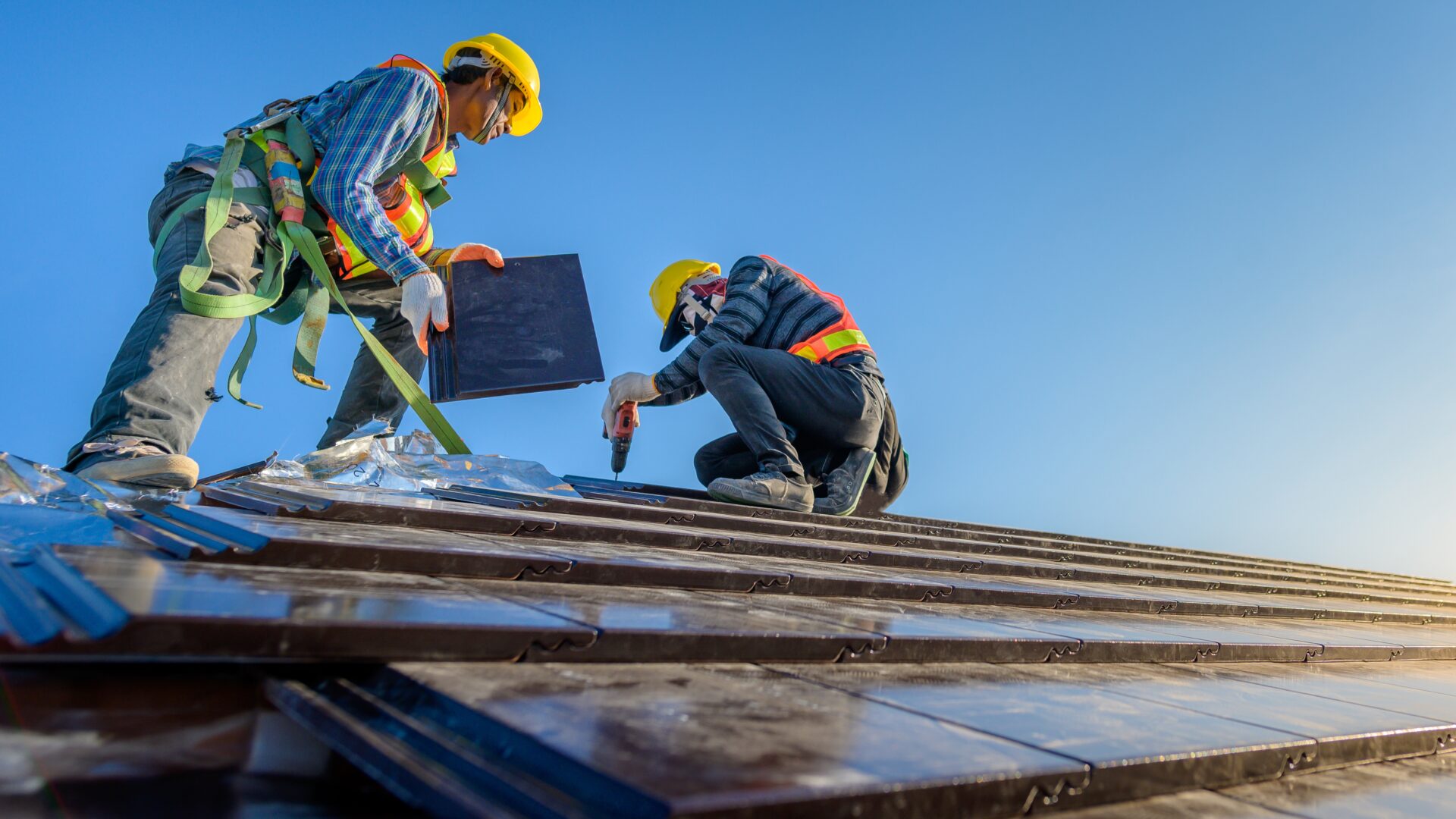 Two roofers in safety gear repair a tile roof