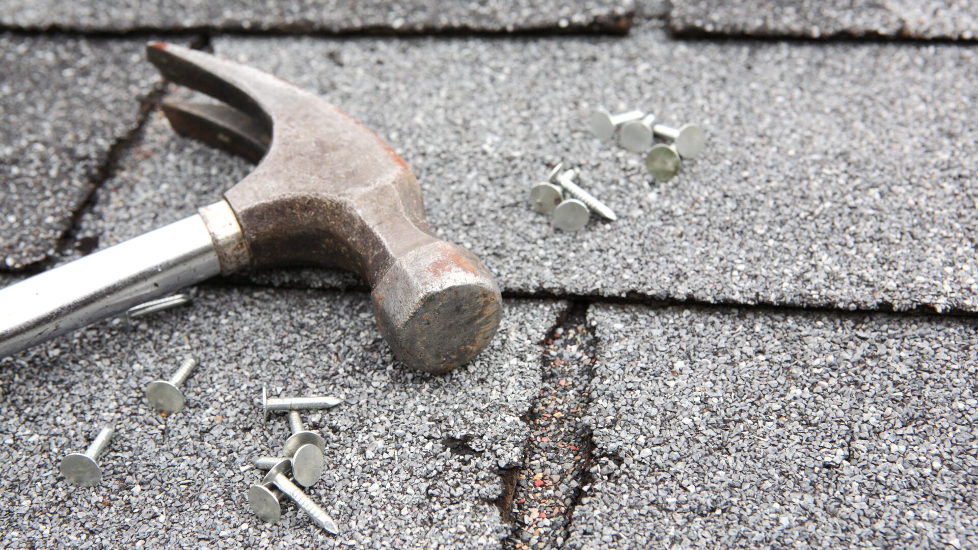 A hammer and roofing nails laying on a shingle roof