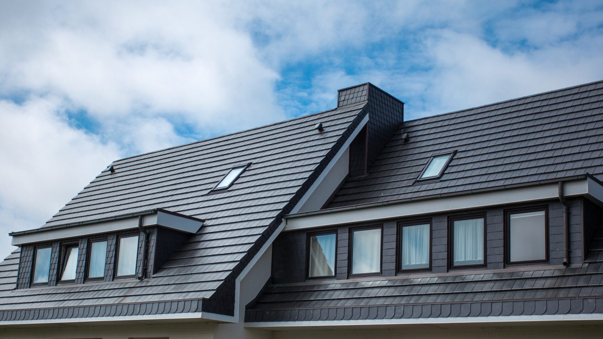 An black tile roof with a dormer window and two skylights